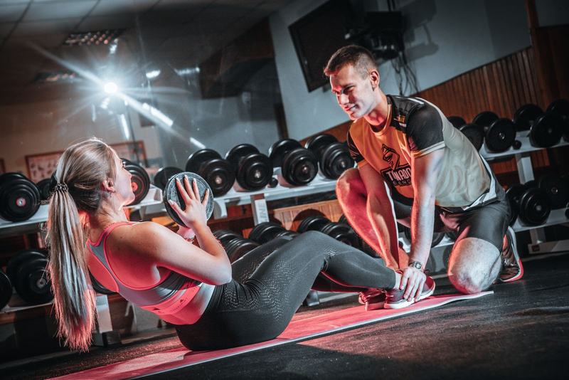 Mulher fazendo abdominal com uma bola em uma academia, com um professor ajudando