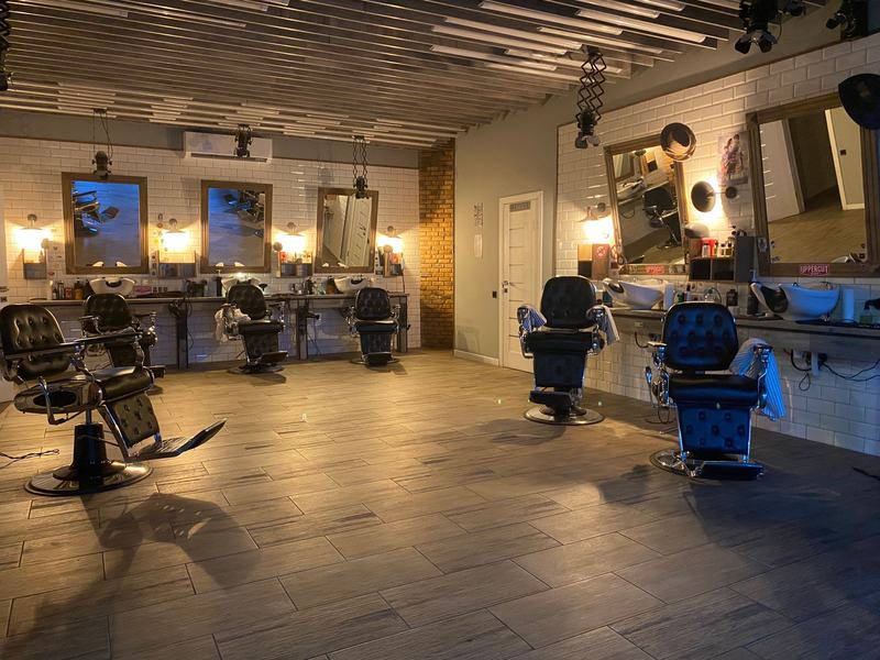 Interior de uma barbearia com cadeiras pretas, espelhos e luz quente