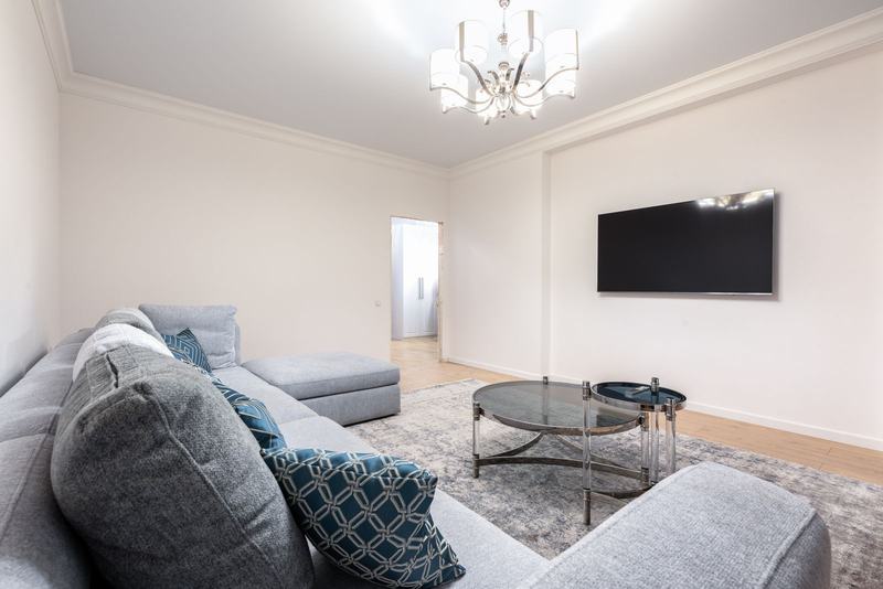 Sala de estar clara com sofá cinza e televisão, em um apartamento moderno