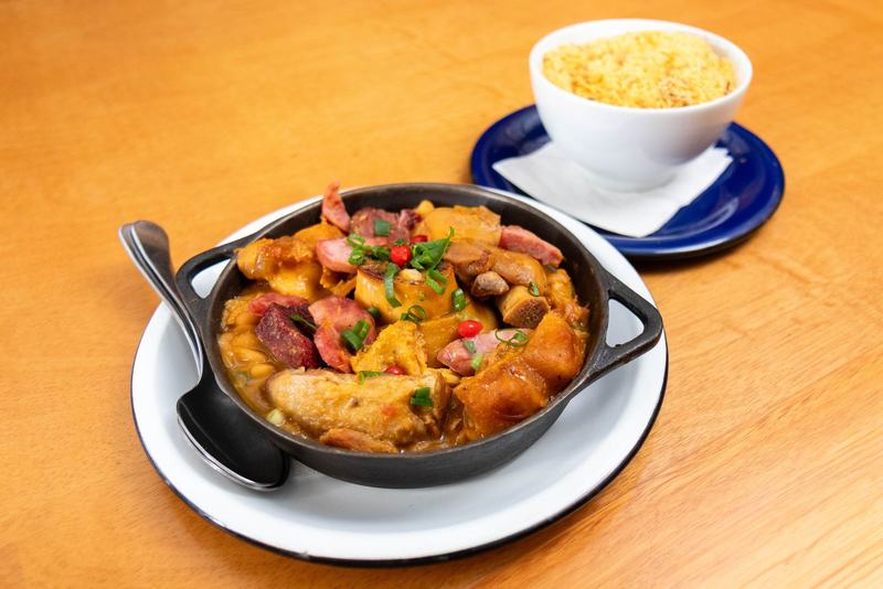 Panela de feijoada brasileira com arroz branco sobre uma mesa de madeira