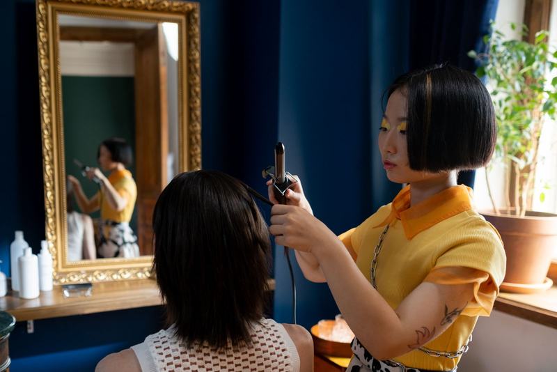 Cabeleireira modelando o cabelo de uma cliente diante de um espelho com moldura dourada